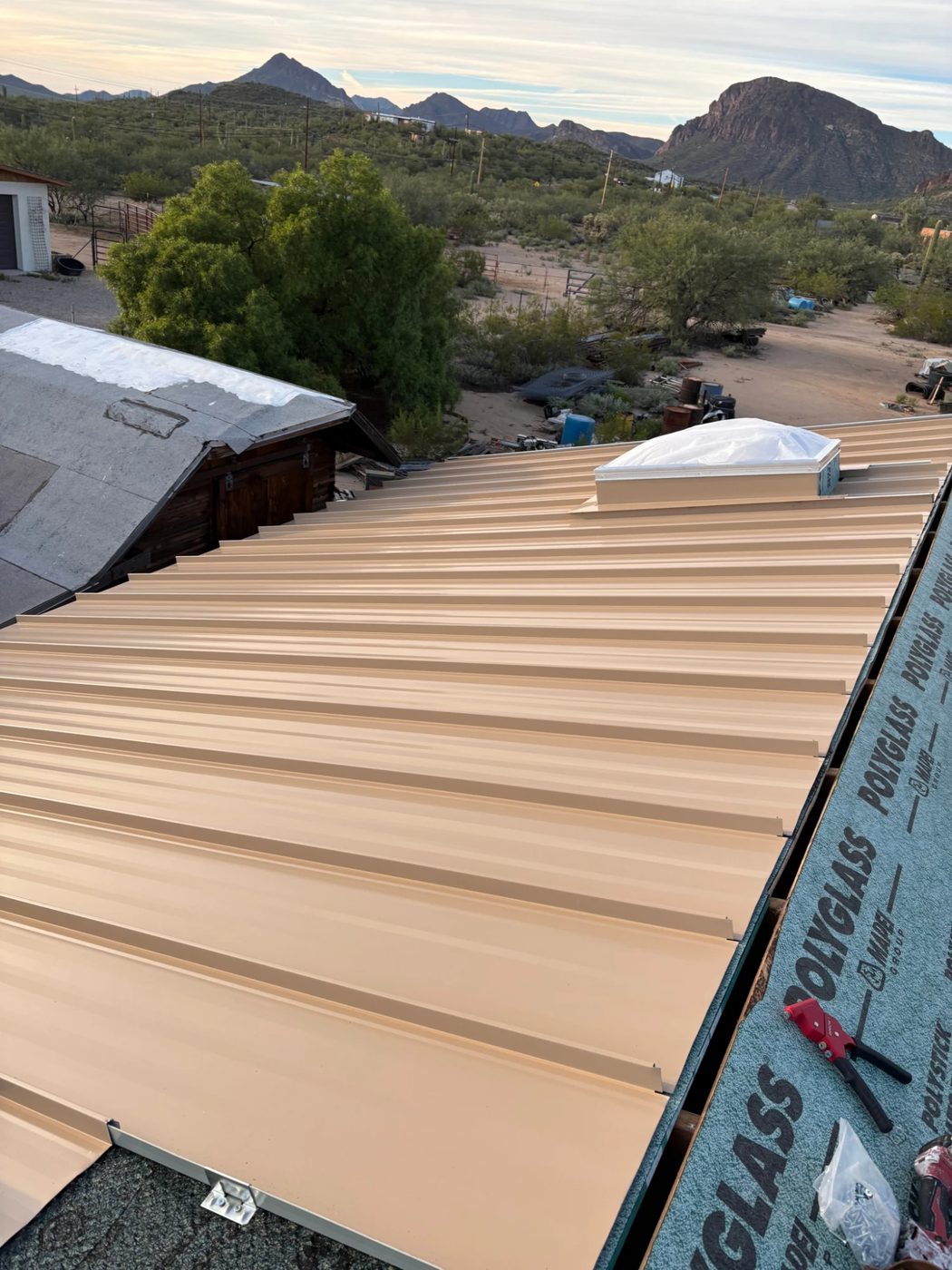 Standing-seam metal roof installation in progress with a skylight curb and Polyglass underlayment along the edge.