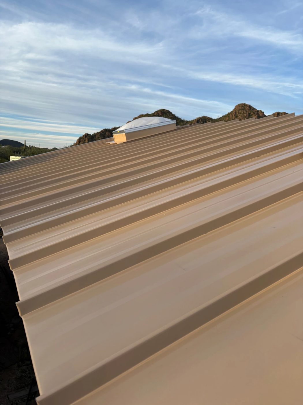 Finished standing-seam metal roof with a skylight, desert mountains beyond.