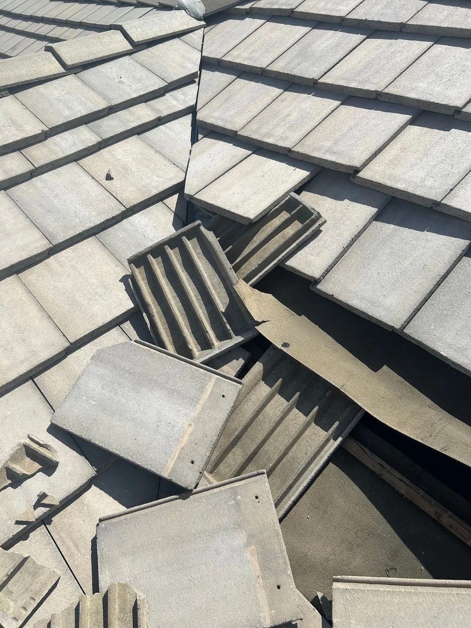 Tile stacked aside with the battens and aged underlayment exposed along a roof valley