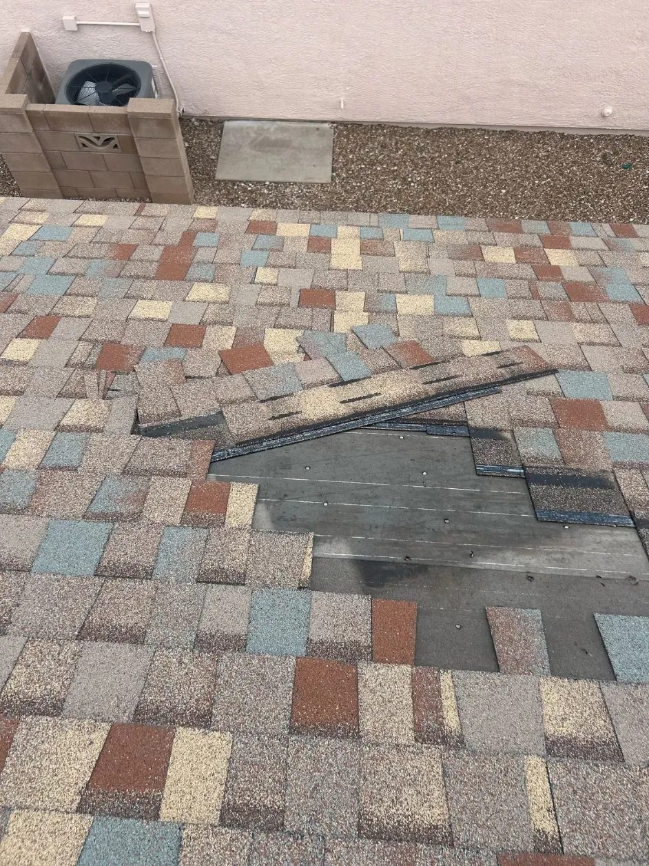 Wind-damaged shingles lifted away from a Tucson roof, exposing the decking beneath