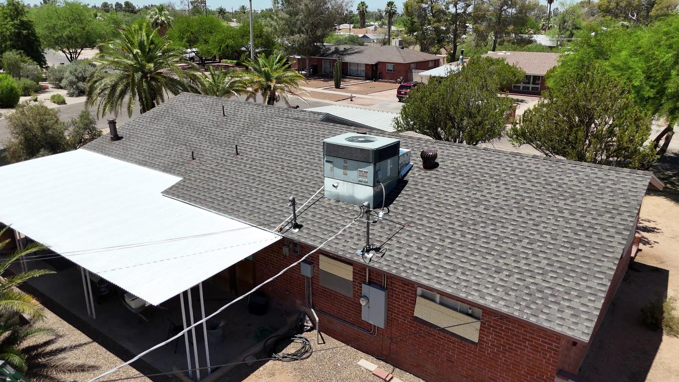 Aerial view of a finished shingle roof adjoining a metal flat roof with white roof coating.