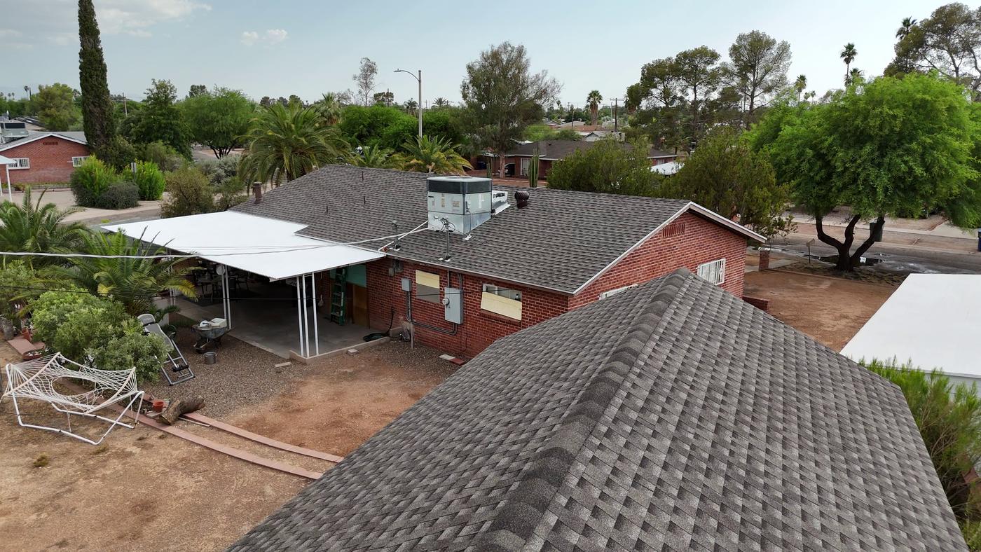Elevated view of a finished shingle roof beside a coated metal flat roof.