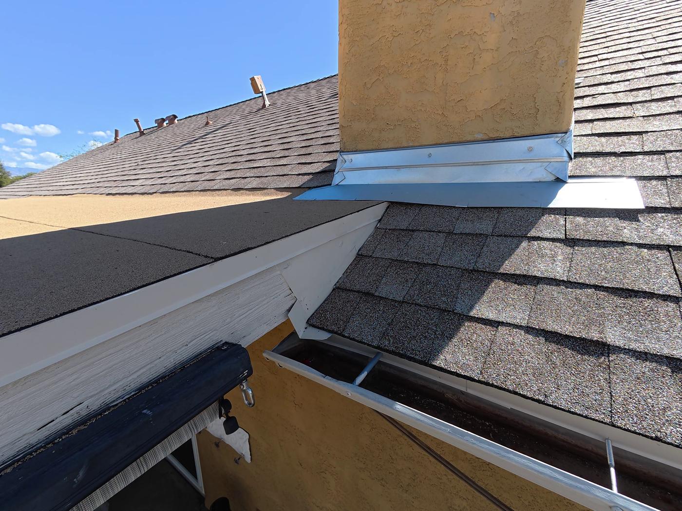 Chimney flashing at the junction of shingles and a low-slope modified bitumen roof.
