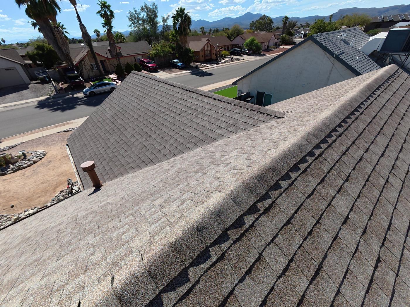 Finished asphalt shingle roof with intersecting roof slopes.