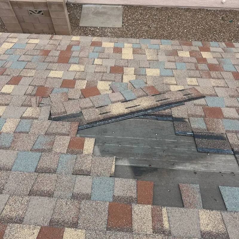 Wind-damaged shingles lifted away from a Tucson roof, exposing the decking beneath